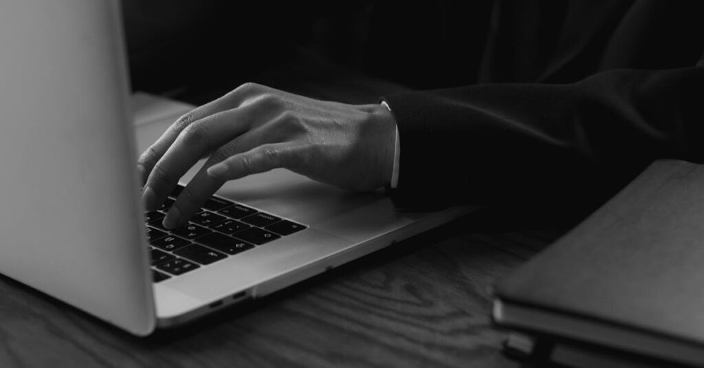 A business professional wearing a suit types on a laptop, captured in a grayscale artistic style.